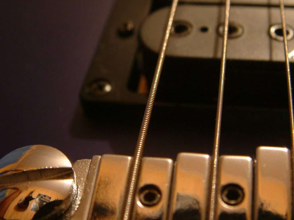 image showing roundwound electric guitar strings in their saddles passing over a pickup
